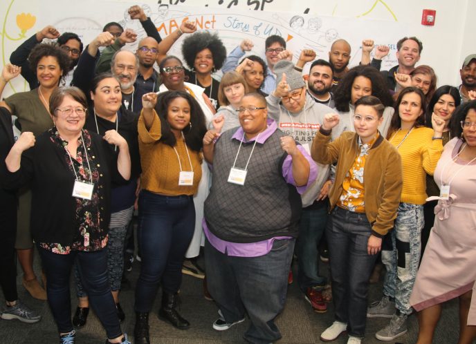 A group photo of the MediaJustice Network in 2018 in Oakland, CA. Many smiling faces with hands raised in a show of collective power.